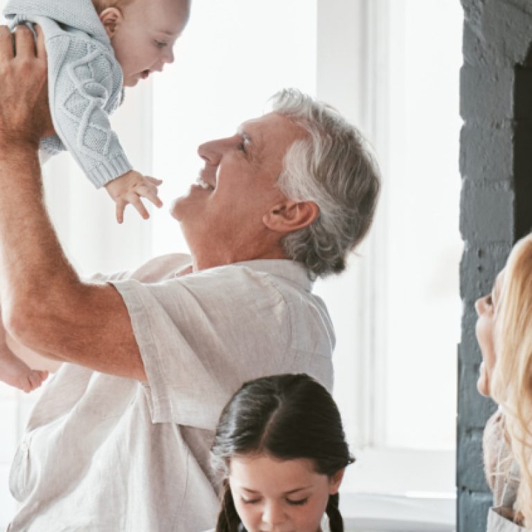 Family, kitchen and grandpa playing with baby having fun, bonding and relax together. Big family, support or care of grandfather carrying newborn with mother, father and girl child cooking in house