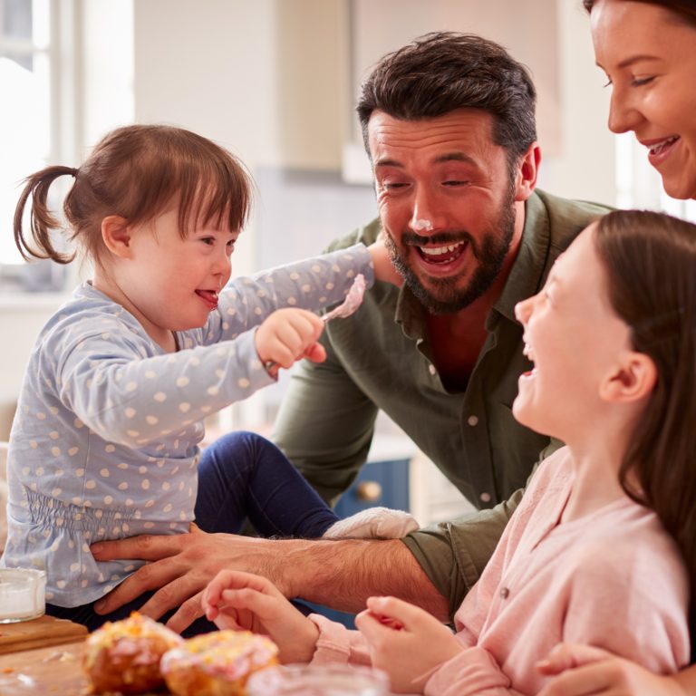 Family With Down Syndrome Daughter Baking And Decorating Cakes Sitting Around Table At Home
