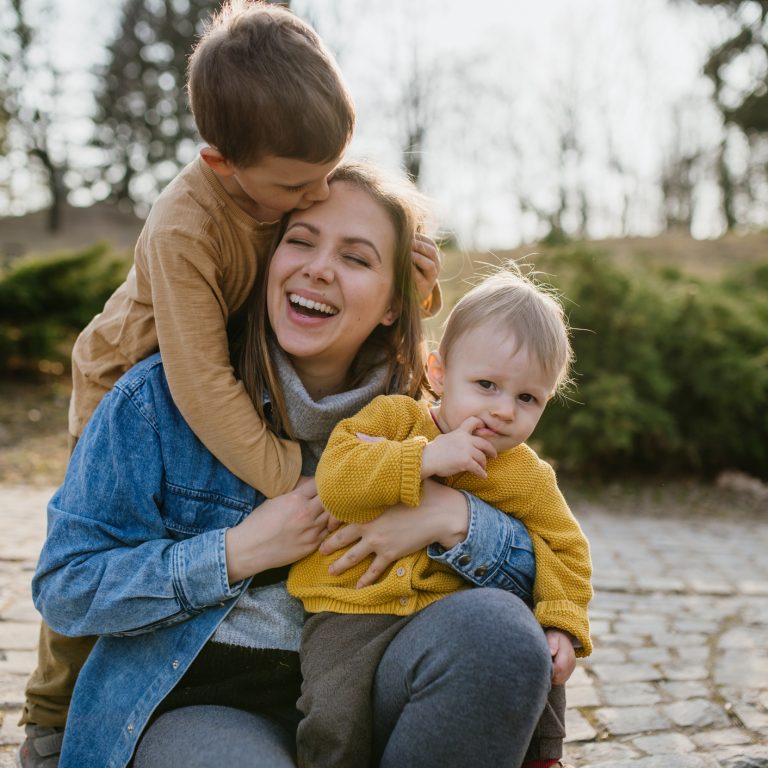 A happy young mother squatting and holding her little children, having fun, laughing in park in autumn.