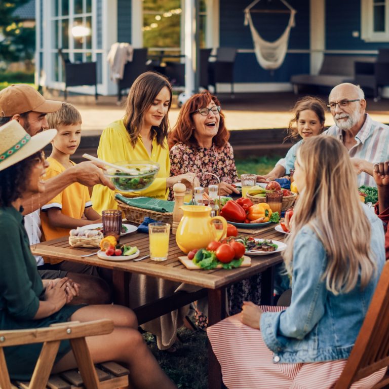 Parents, Children, Relatives and Friends Having an Open Air Vegetarian Dinner in Their Backyard. Old and Young People Talk, Chat, Have Fun, Eat and Drink. Garden Party Celebration in a Backyard.