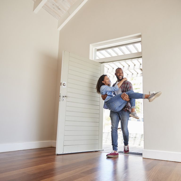Man Carrying Woman Over Threshold Of Doorway In New Home