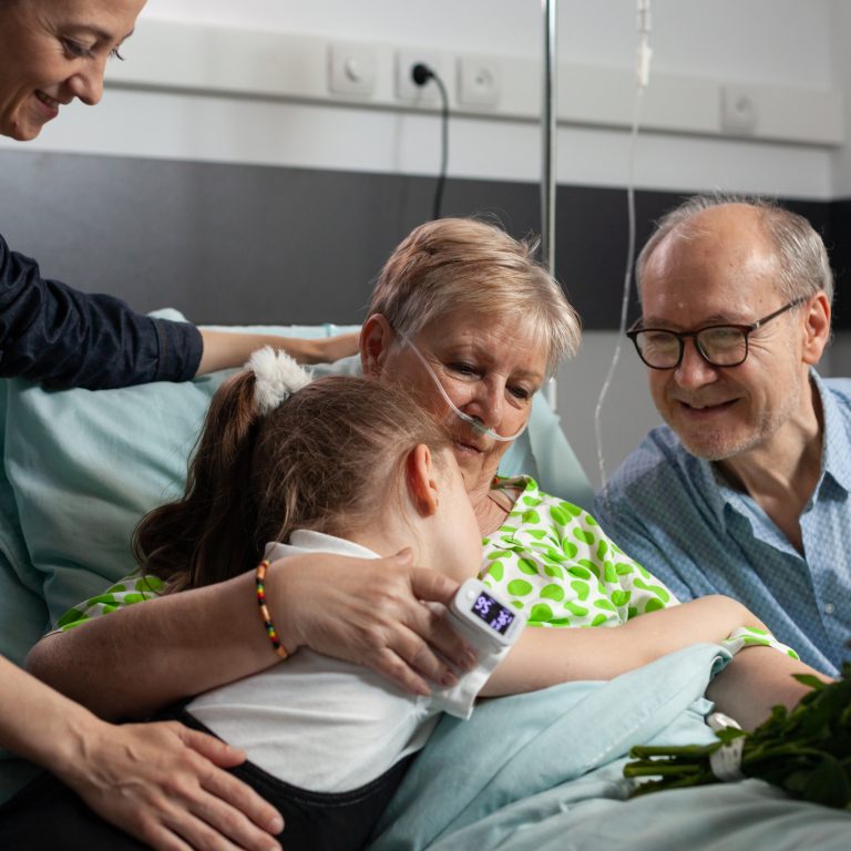 Little granddaughter bringing flowers while visiting sick grandmother supporting her after medical surgery during medicine therapy. Child hugging sick senior woman patient visiting in hospital ward